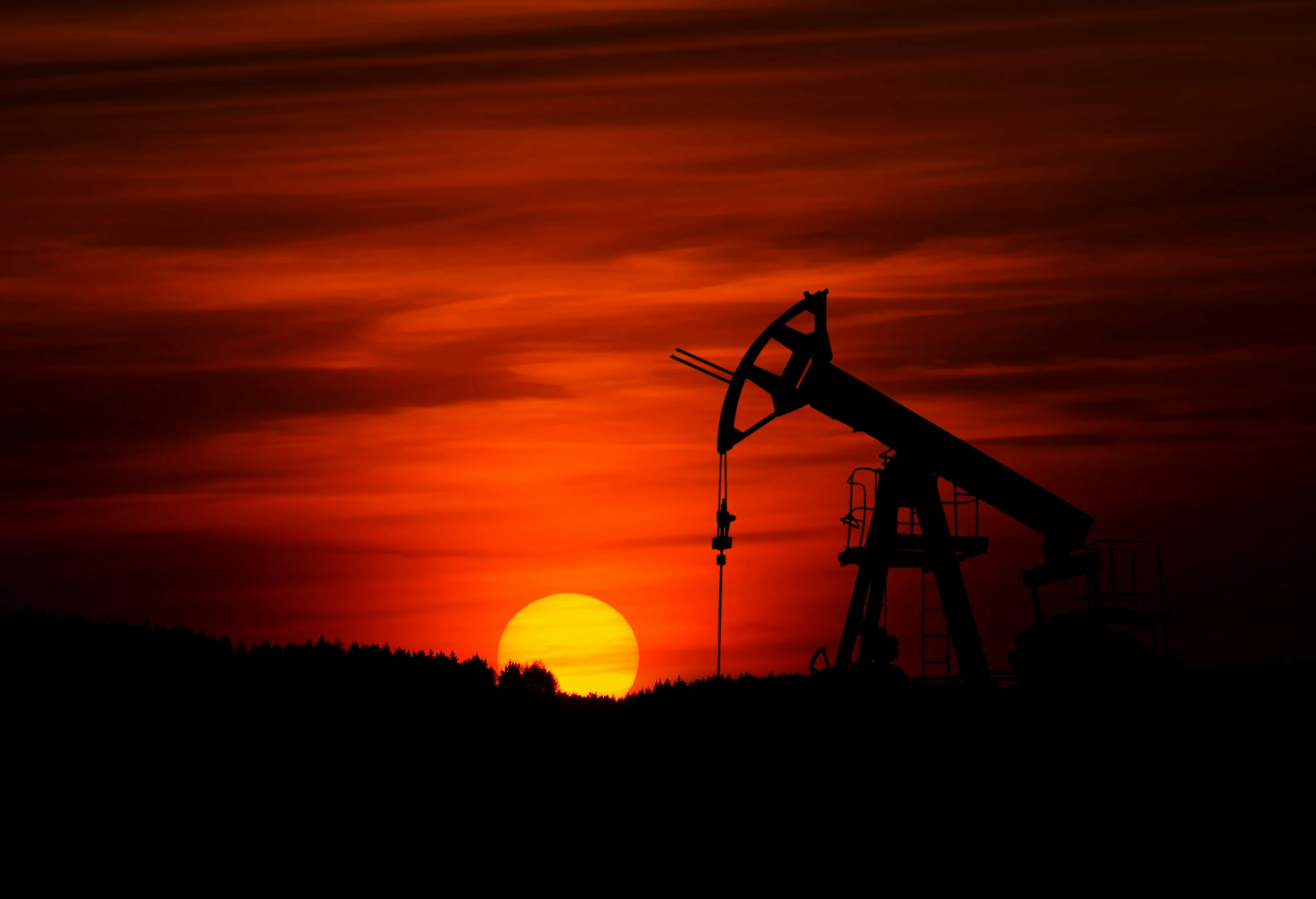 Oil pump jack silhouetted against a dramatic sunset over open Texas terrain